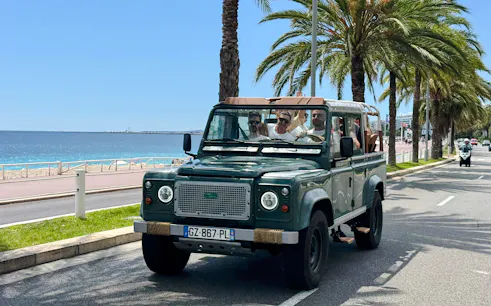 Land Rover driving along Nice's coastal road with palm trees and sea view.