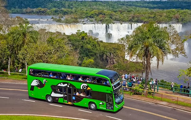 Green tour bus near Brazilian Falls with tourists viewing the waterfall.