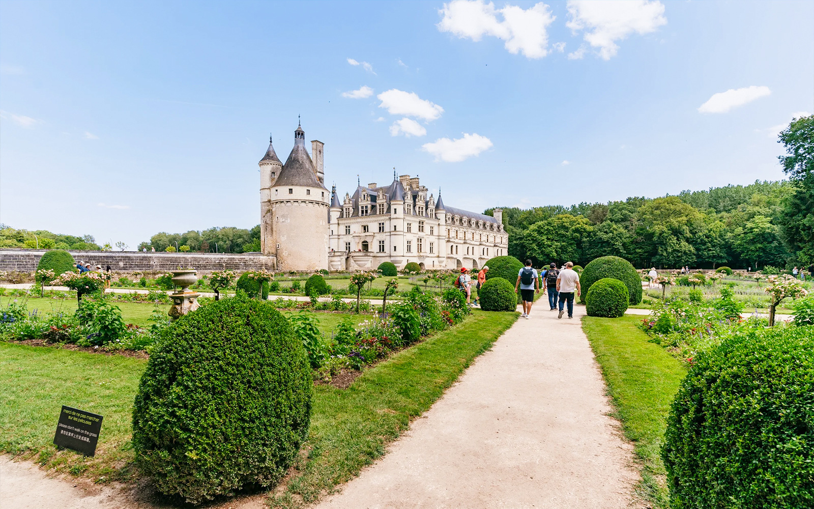 Visitors walking through gardens towards Chateau de Chenonceau, France.