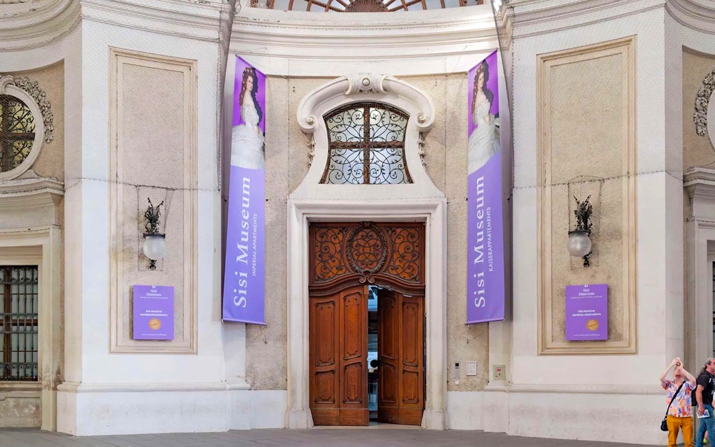 Entrance to the Sisi Museum with ornate wooden doors and purple banners in Vienna.