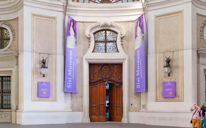 Entrance to the Sisi Museum with ornate wooden doors and purple banners in Vienna.