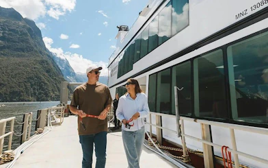 Couple boarding a cruise ship at Milford Sound with scenic mountain views.