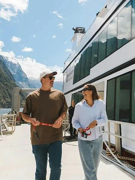 Couple boarding a cruise ship at Milford Sound with scenic mountain views.