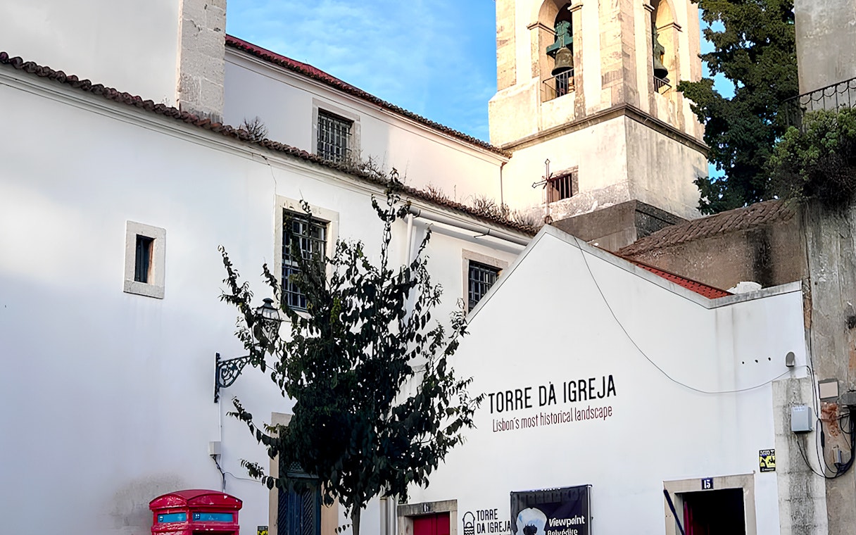 Tower of St. George's Castle Church in Lisbon with bell tower and white facade.