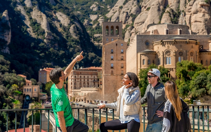 Guide pointing out Montserrat views to tourists in front of monastery.