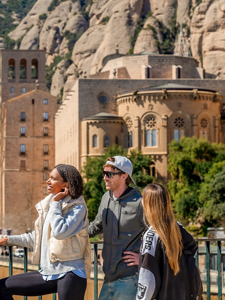 Guide pointing out Montserrat views to tourists in front of monastery.