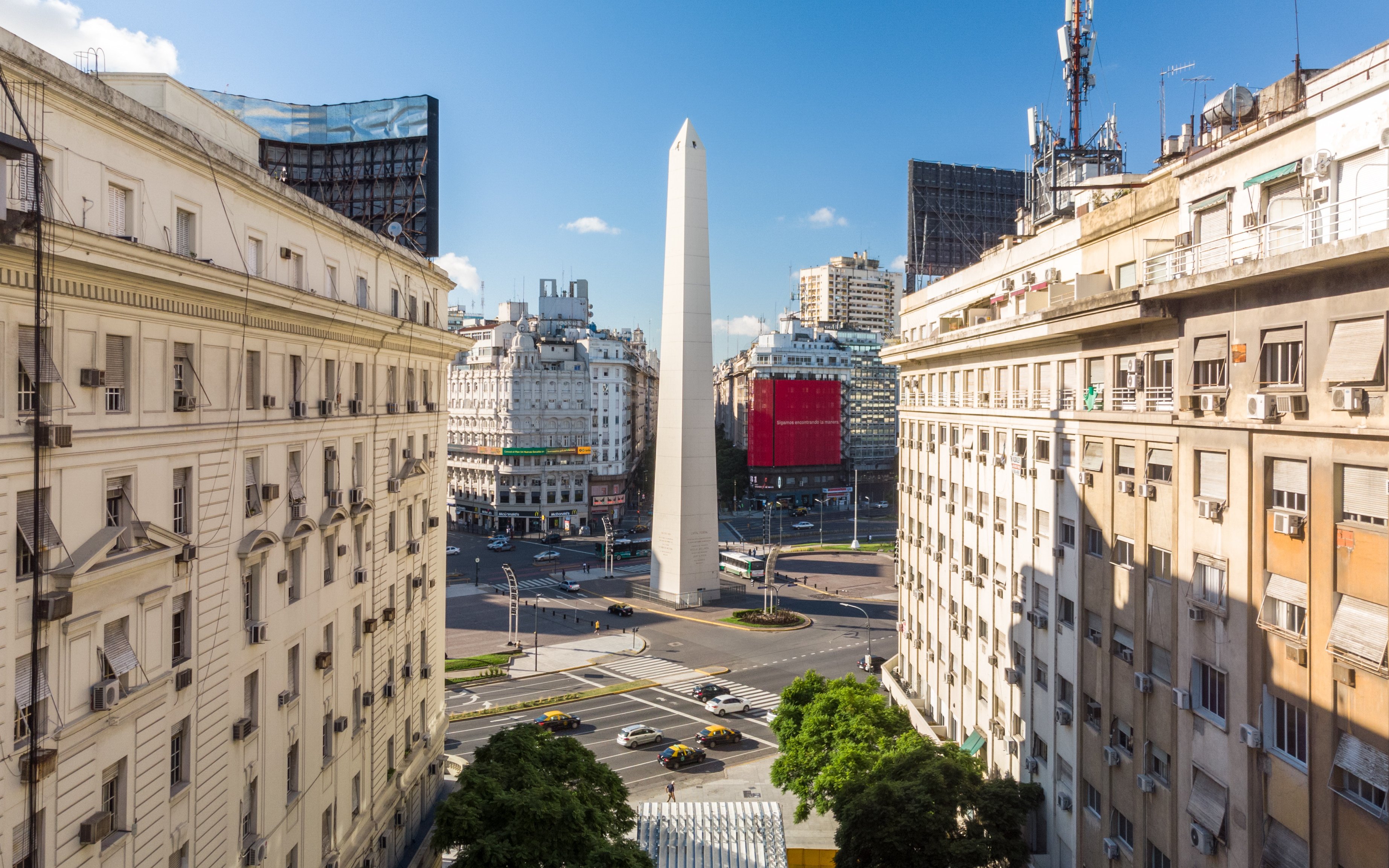 Obelisk of Buenos Aires between colonial buildings on 9 de Julio Avenue under blue sky.