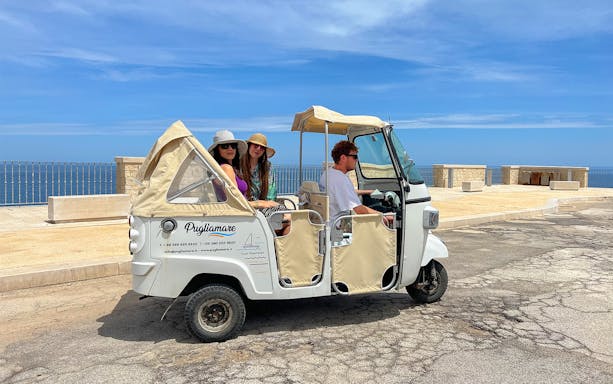 Tuk-tuk with passengers on coastal tour in Polignano a Mare, Italy.