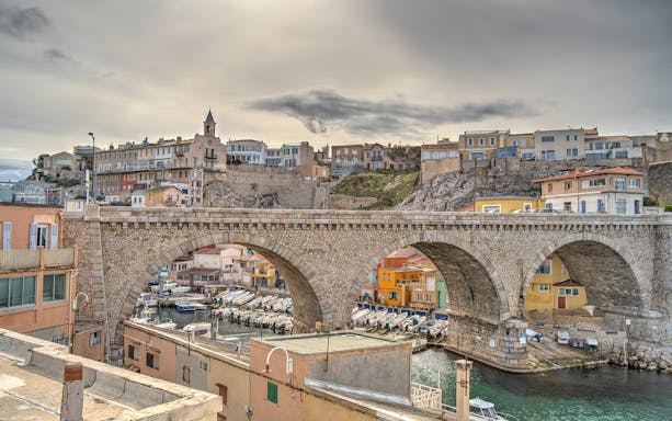 Marseille sea district bridge with boats and hillside homes in city exploration game.