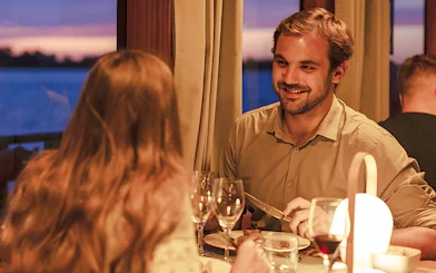 Couple dining on Bateaux Bordelais dinner cruise with sunset view.
