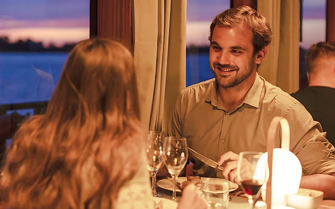 Couple dining on Bateaux Bordelais dinner cruise with sunset view.