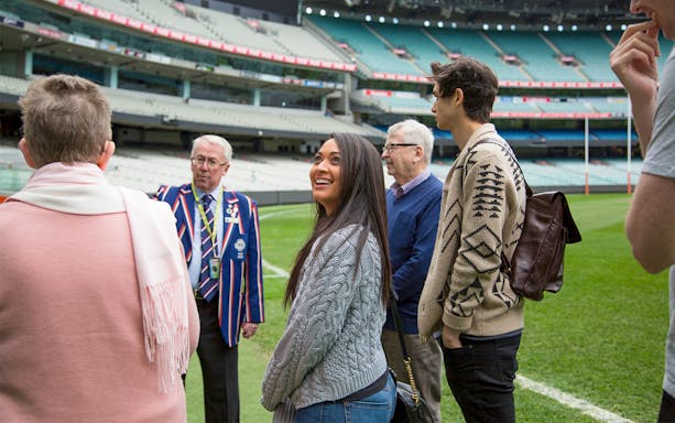 Group on Melbourne Cricket Ground tour with guide in colorful blazer.