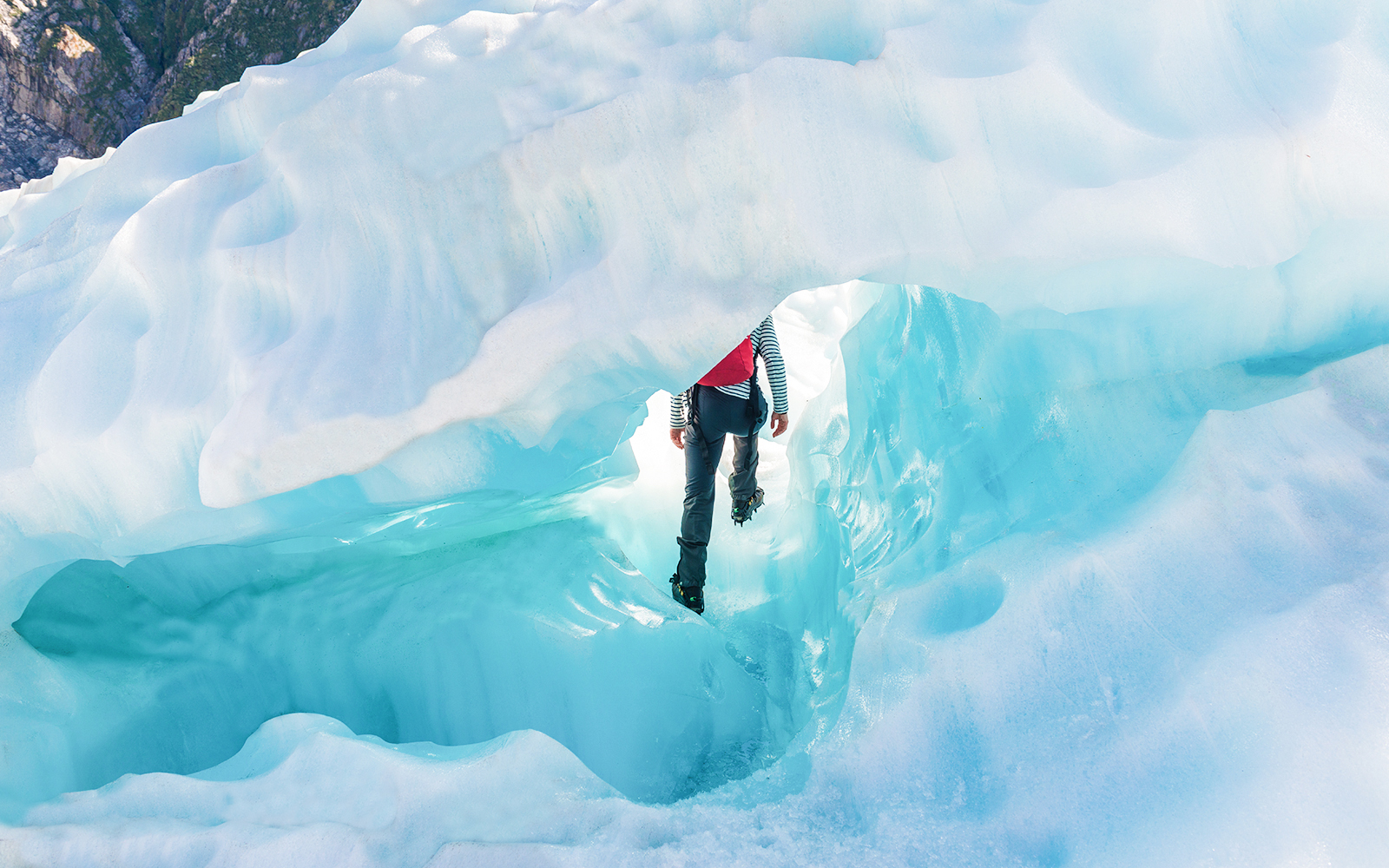 Person hiking through ice cave on Fox Glacier, New Zealand, during guided helicopter tour.