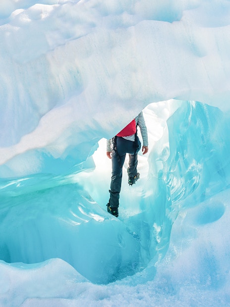 Person hiking through ice cave on Fox Glacier, New Zealand, during guided helicopter tour.
