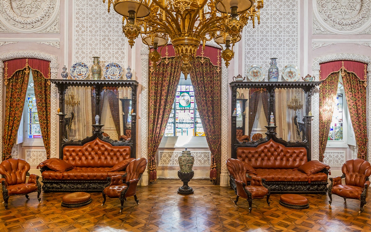 Great Hall of Pena Palace with ornate chandelier, stained glass window, and antique furniture.
