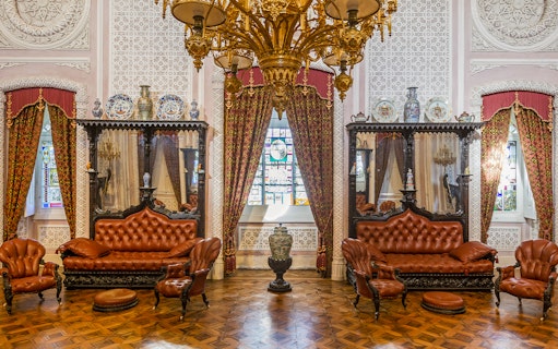Great Hall of Pena Palace with ornate chandelier, stained glass window, and antique furniture.