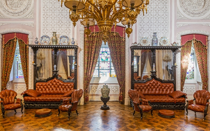 Great Hall of Pena Palace with ornate chandelier, stained glass window, and antique furniture.