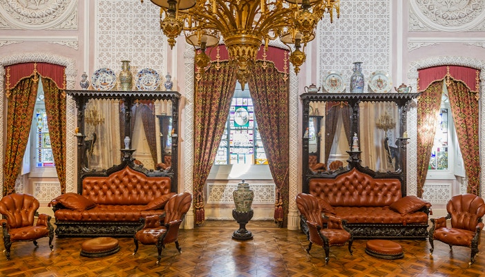 Great Hall of Pena Palace with ornate chandelier, stained glass window, and antique furniture.