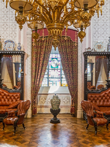 Great Hall of Pena Palace with ornate chandelier, stained glass window, and antique furniture.