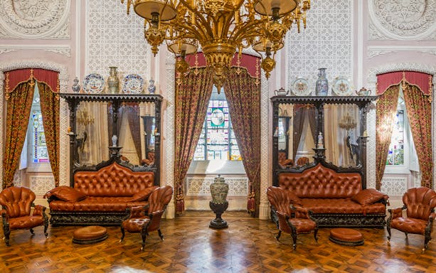 Great Hall of Pena Palace with ornate chandelier, stained glass window, and antique furniture.