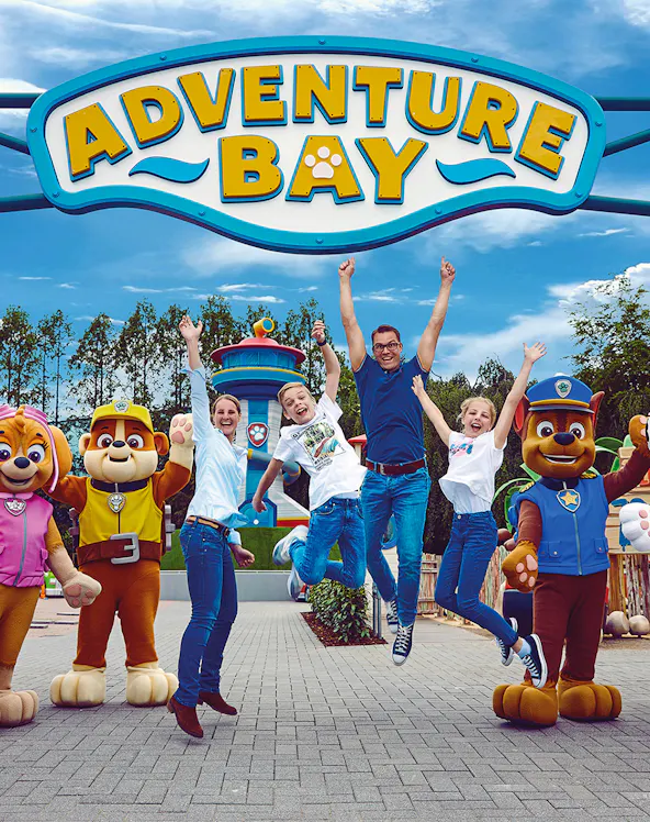 Visitors jumping with joy at Adventure Bay entrance in Movie Park, surrounded by character mascots.