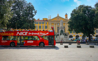 Hop-on hop-off bus in Nice, France, near a historic building and statue.