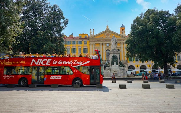 Hop-on hop-off bus in Nice, France, near a historic building and statue.