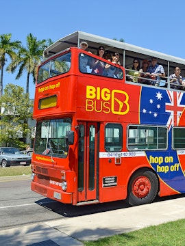 Red double-decker bus with tourists on a hop-on hop-off tour in Darwin, Australia.
