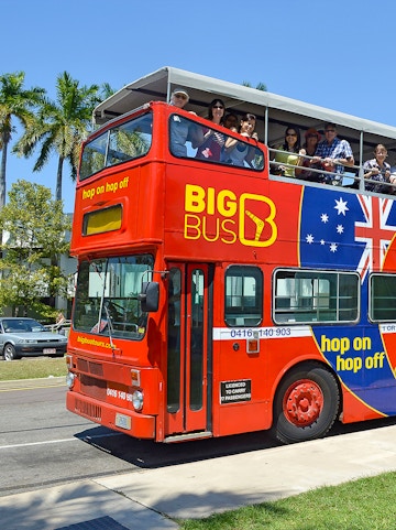 Red double-decker bus with tourists on a hop-on hop-off tour in Darwin, Australia.