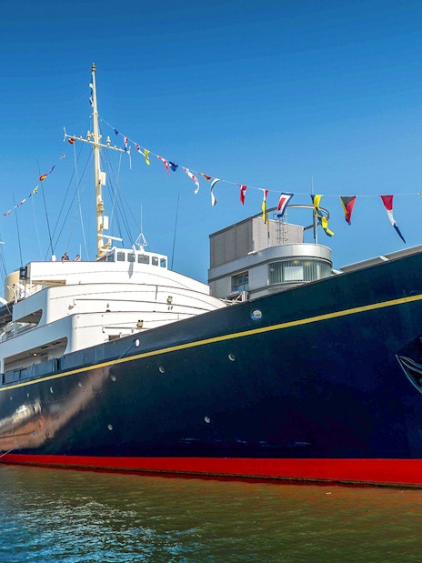 Royal Yacht Britannia docked in Edinburgh with colorful flags.
