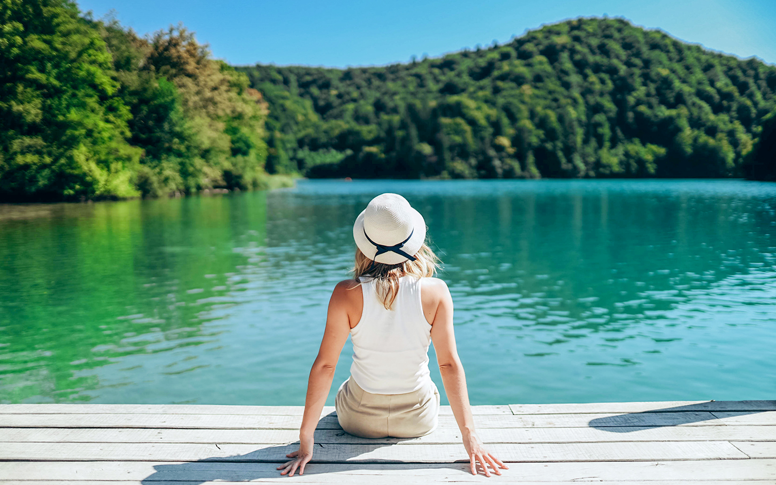 Girl sitting on a wooden bridge over turquoise waters at Plitvice Lakes, Croatia.