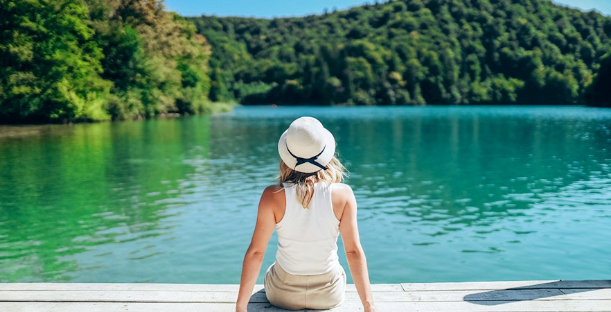 Girl sitting on a wooden bridge over turquoise waters at Plitvice Lakes, Croatia.