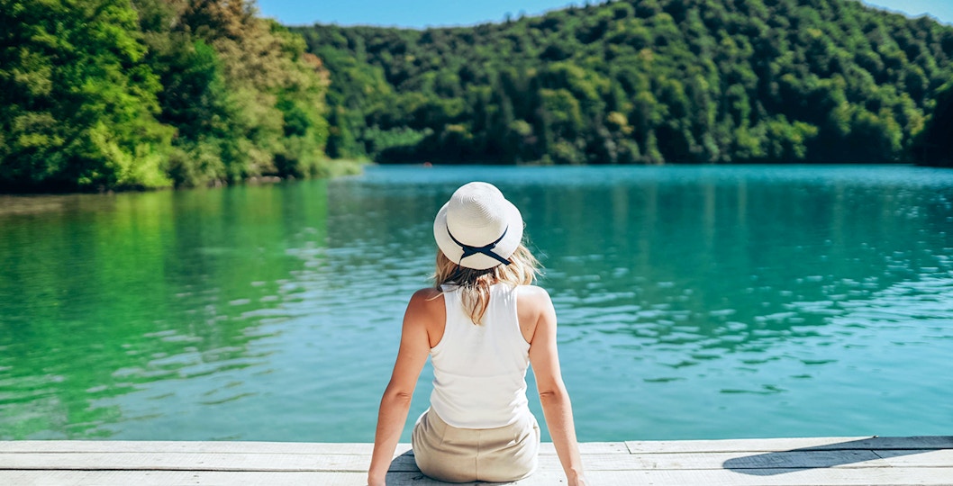 Girl sitting on a wooden bridge over turquoise waters at Plitvice Lakes, Croatia.