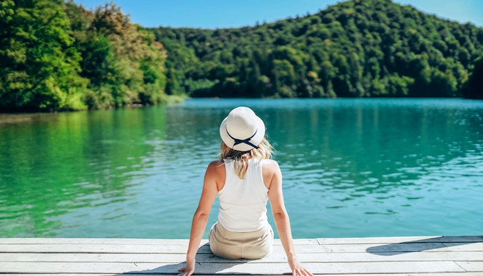 Girl sitting on a wooden bridge over turquoise waters at Plitvice Lakes, Croatia.