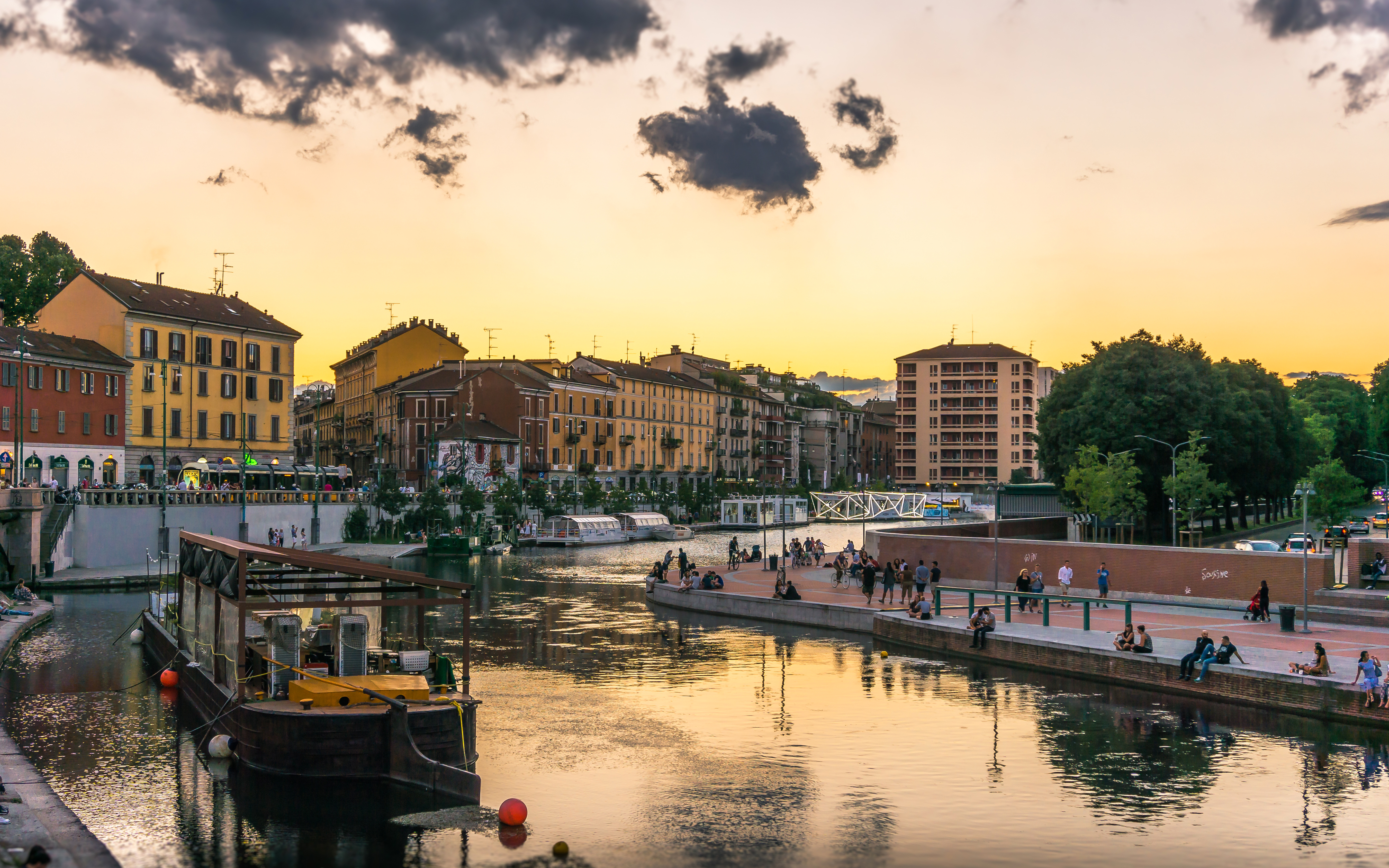 Navigli canals in Milan at sunset with people walking along the waterfront.