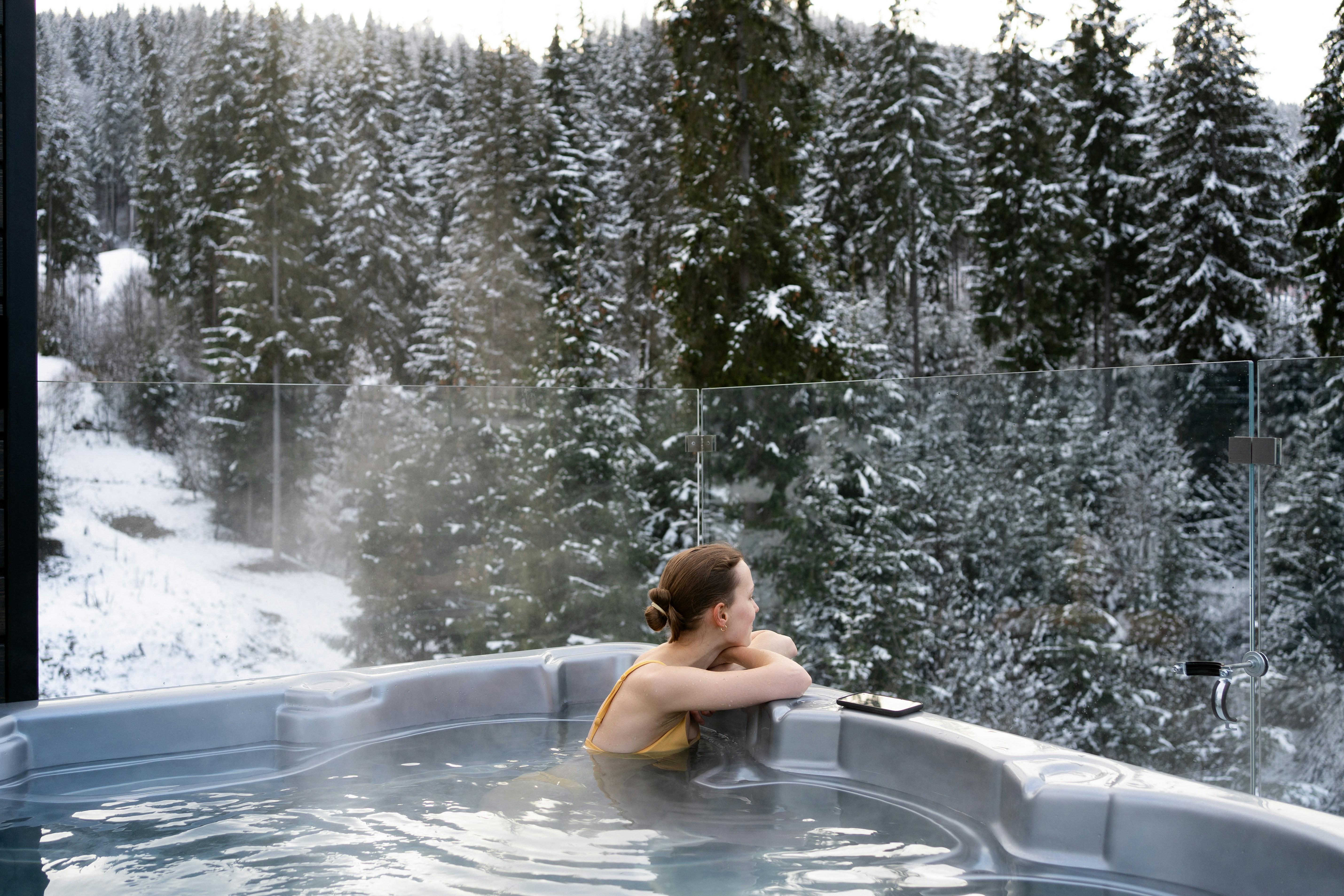 Young woman relaxing in a hot tub overlooking snowy forest.