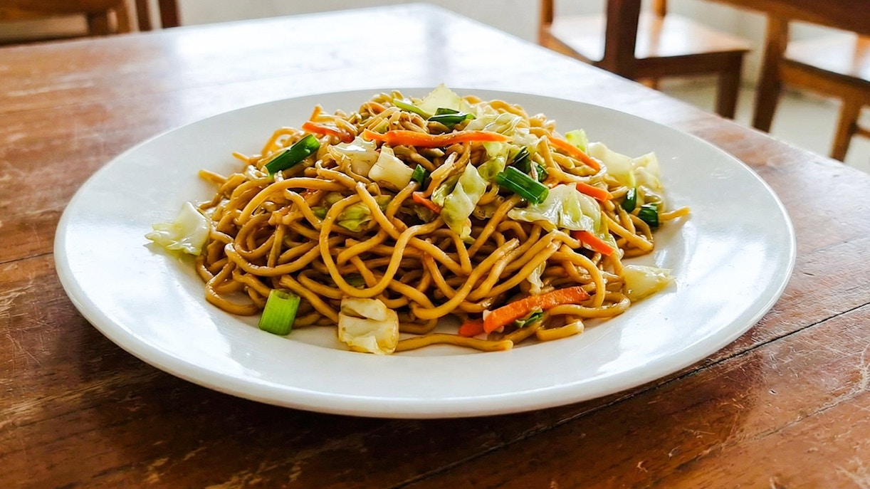 Indonesian fried noodles with vegetables on a white plate.