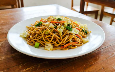 Indonesian fried noodles with vegetables on a white plate.