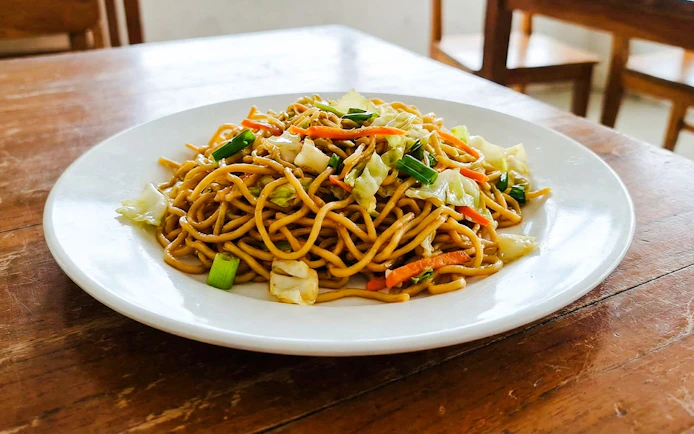 Indonesian fried noodles with vegetables on a white plate.