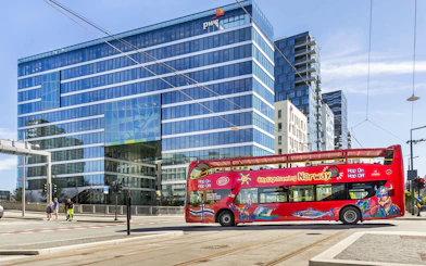 Red City Sightseeing bus in front of modern glass building in Oslo.