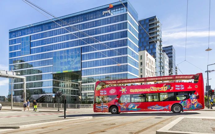 Red City Sightseeing bus in front of modern glass building in Oslo.