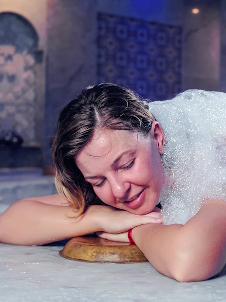 Young woman enjoying foam massage in Turkish bath.