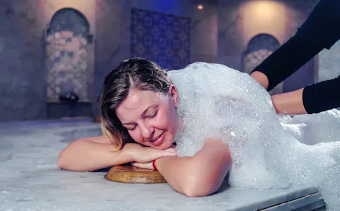 Young woman enjoying foam massage in Turkish bath.
