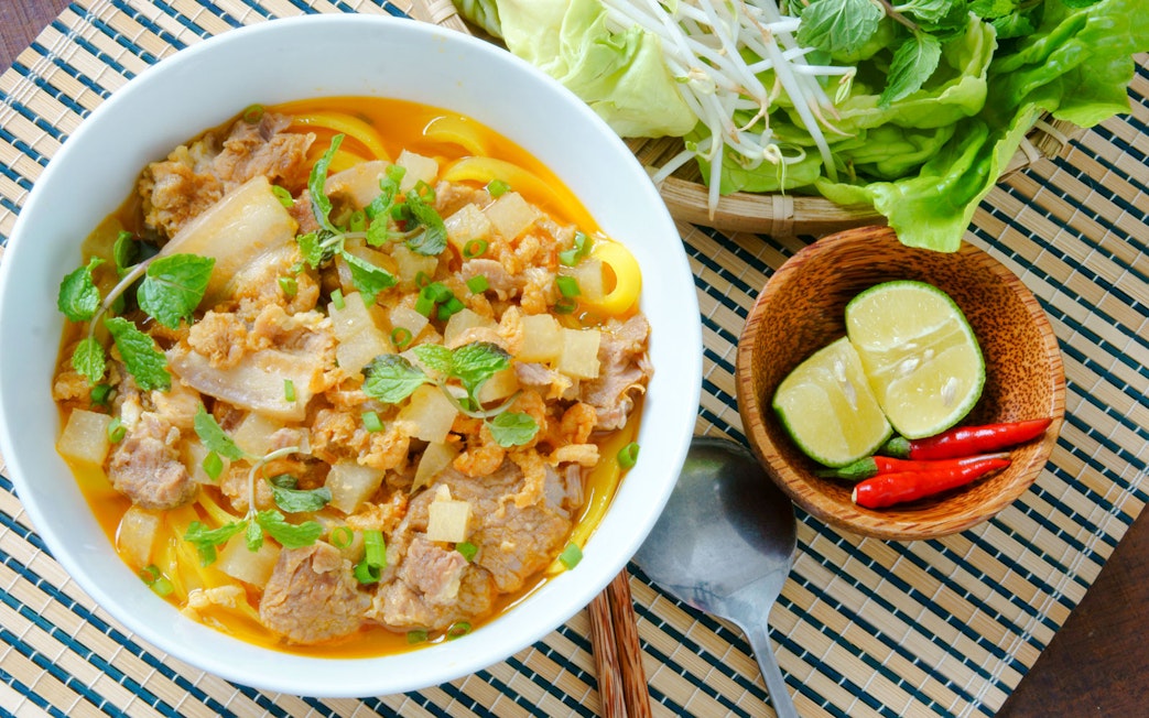 Mi quang noodle dish with pork, herbs, and lime on a woven mat.