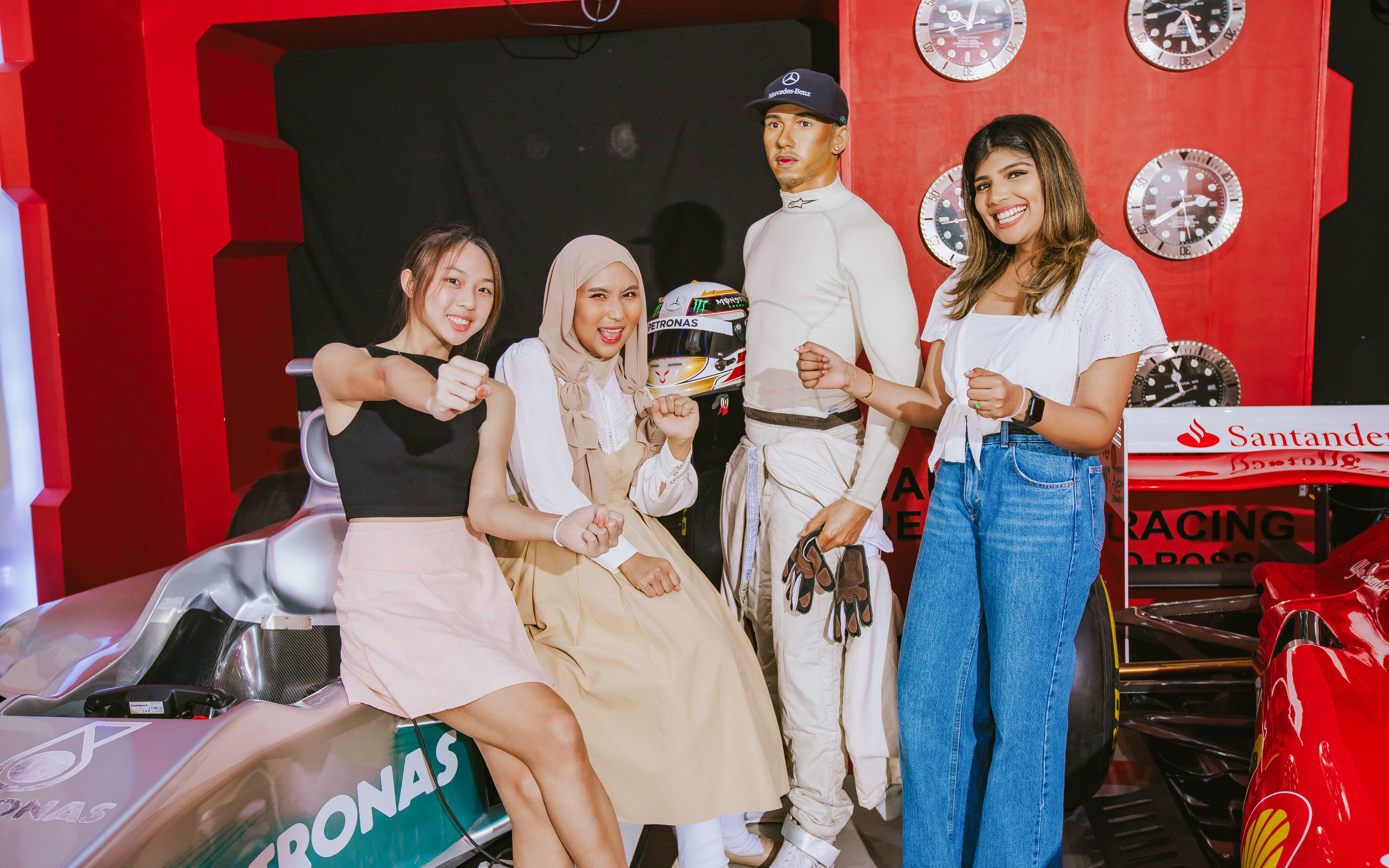 Visitors posing with Lewis Hamilton wax figure at Madame Tussauds London, near a race car display.