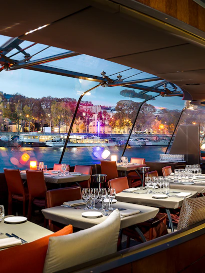 Dining area on a Seine River cruise boat with city view through large windows.