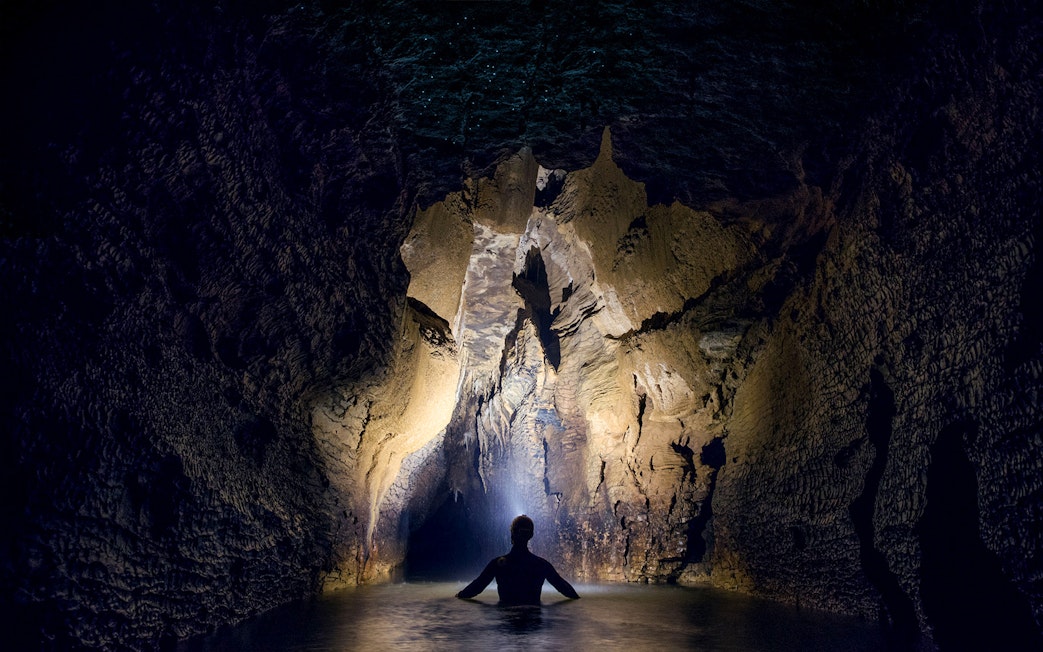 Person exploring illuminated cave during black water rafting in Waitomo.