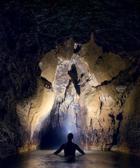 Person exploring illuminated cave during black water rafting in Waitomo.
