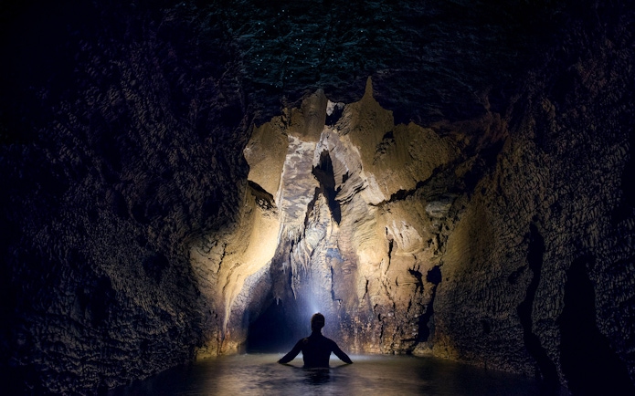 Person exploring illuminated cave during black water rafting in Waitomo.