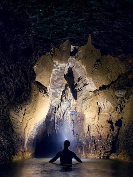 Person exploring illuminated cave during black water rafting in Waitomo.